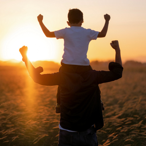 Sohn auf den Schultern des Vaters. Beide ballen die Fäuste zum Himmel
